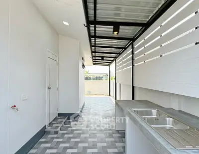 Modern outdoor kitchen with sleek design and tiled flooring, featuring a stainless steel sink and covered roof.