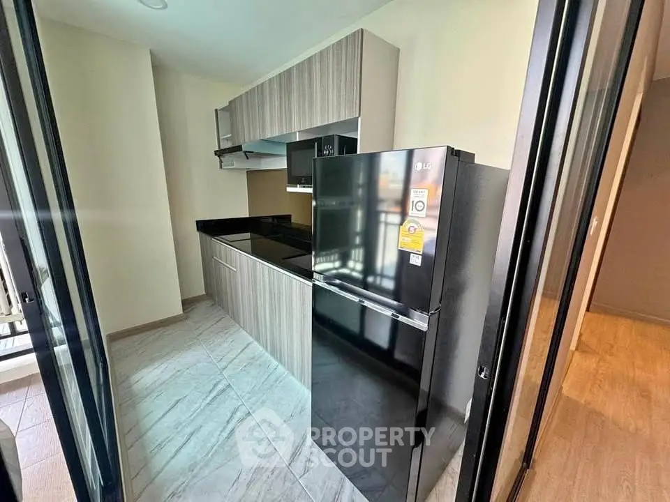 Modern kitchen with sleek cabinetry and black refrigerator in a compact layout.