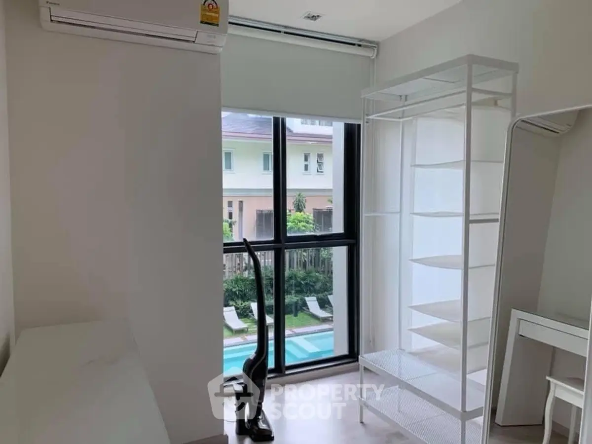 Bright room with large window overlooking pool, featuring modern shelving and air conditioning.