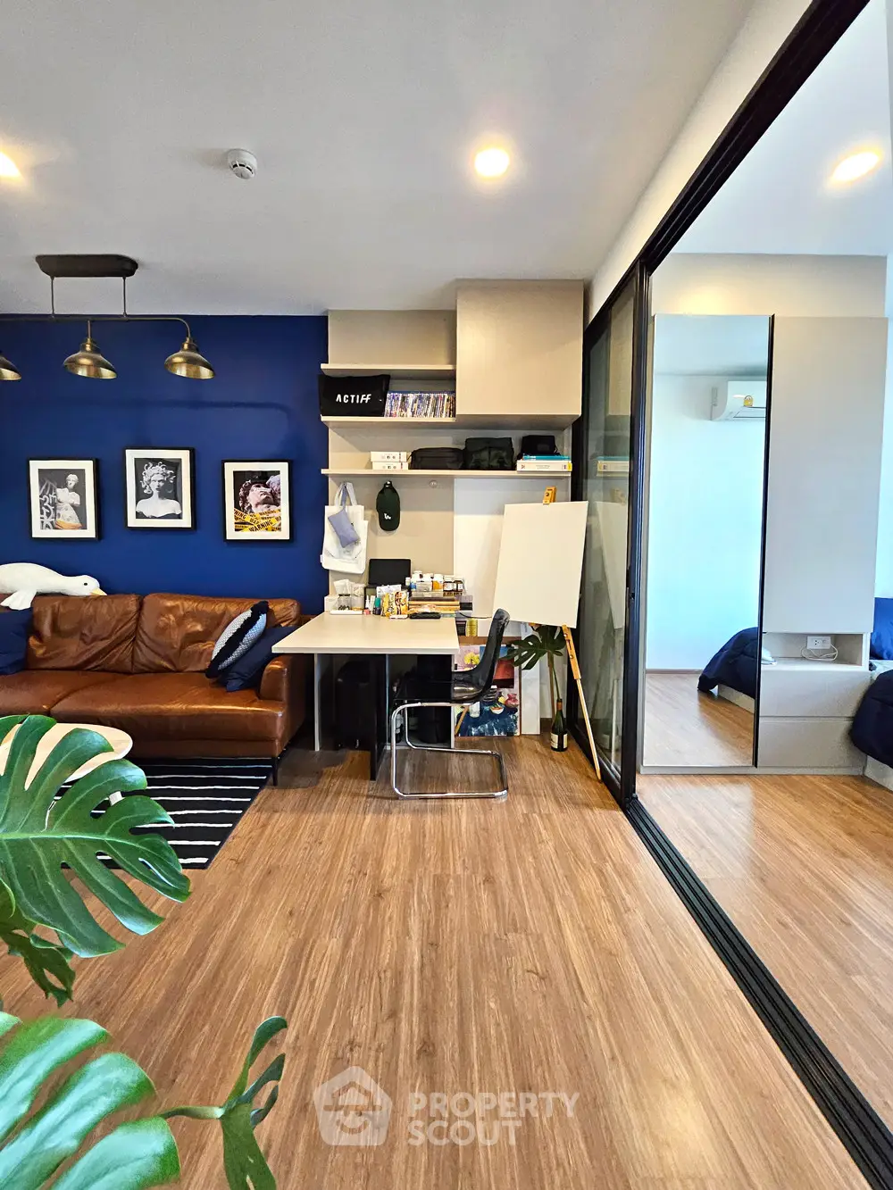 Modern living room with stylish decor and open layout, featuring a cozy workspace and sliding glass doors to bedroom.