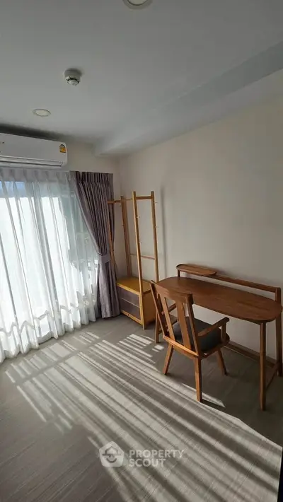 Bright study room with wooden desk and chair, large window with curtains, and ample natural light.