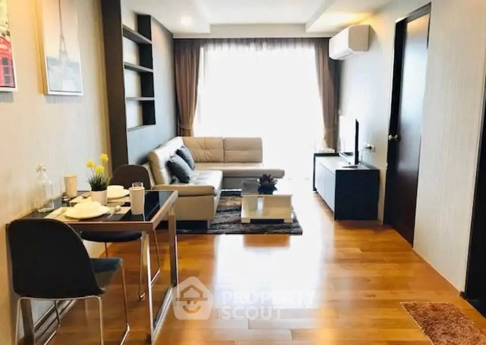 Modern living room with wooden flooring, stylish furniture, and natural light from large window.