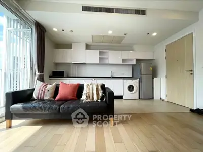 Modern open-layout living room with sleek kitchen and washing machine, featuring stylish sofa and wooden flooring.