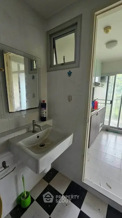 Modern bathroom with sleek sink and mirror, leading to a bright kitchen with large windows.