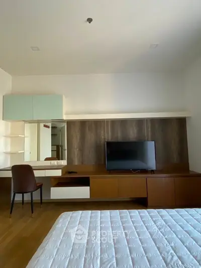 Modern bedroom with sleek furniture and mounted TV, featuring a cozy workspace.