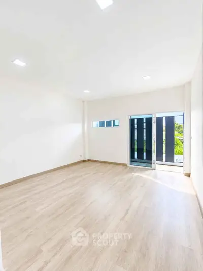 Spacious empty room with wooden flooring and large window offering natural light and garden view.