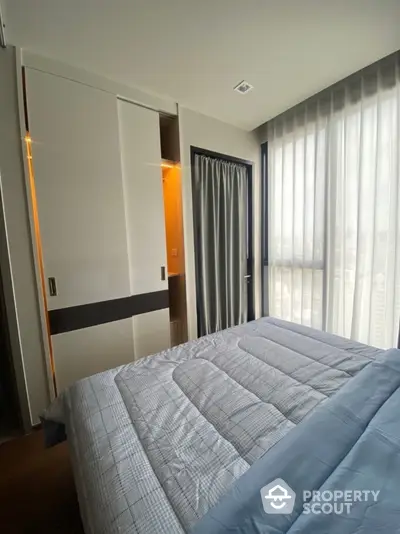 Modern bedroom with large window and stylish bedding in a contemporary apartment.