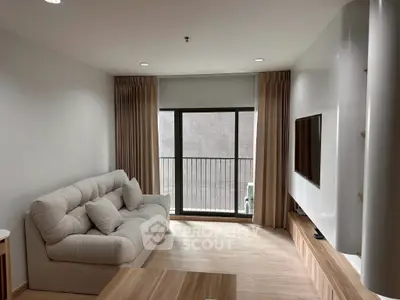 Modern living room with cozy sofa and large TV, featuring natural light from balcony window.