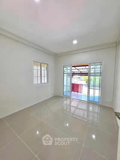 Spacious room with glossy tiled floors and large windows leading to a covered outdoor area.