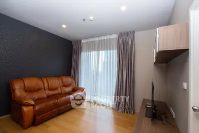 Modern living room with leather sofa and TV, featuring elegant curtains and wooden flooring.