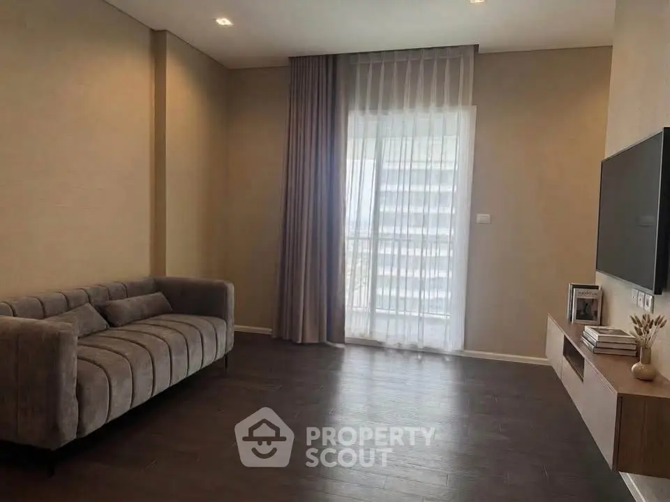 Modern living room with sleek sofa and wall-mounted TV, featuring floor-to-ceiling window drapes.