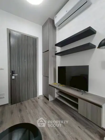 Modern living room with sleek furniture and wall-mounted TV, featuring a minimalist design and air conditioning.