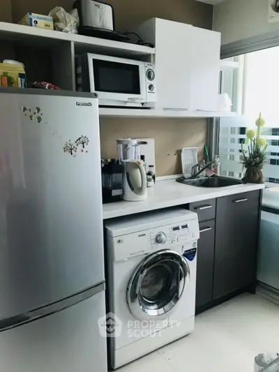 Modern kitchen with appliances including fridge, microwave, and washing machine in compact layout.