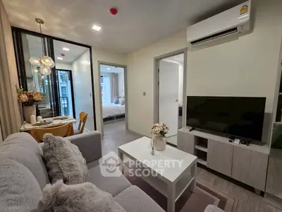 Modern living room with cozy decor and open view to bedroom, featuring sleek furniture and air conditioning.