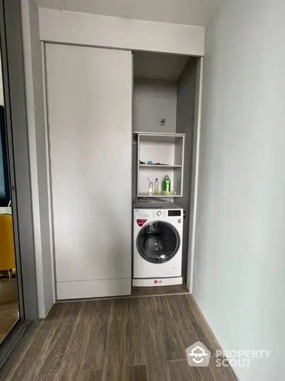 Modern laundry area with washing machine and storage shelves in sleek apartment.