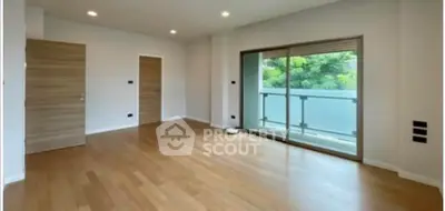 Spacious empty room with wooden flooring and large balcony access.