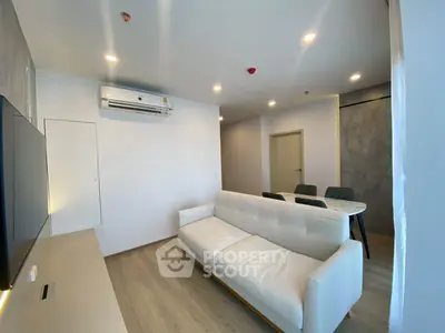 Modern living room with sleek white sofa and dining area, featuring contemporary lighting and air conditioning.