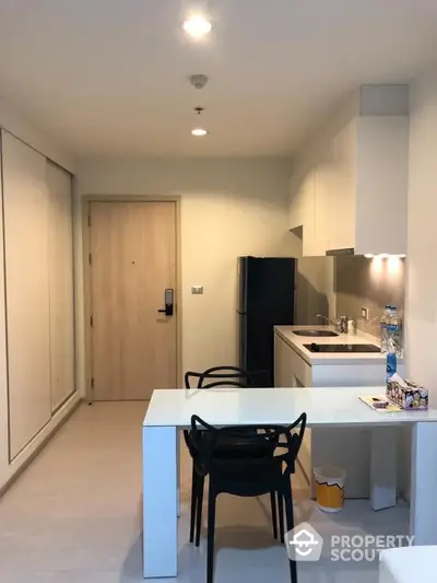 Modern kitchen with sleek white cabinets and dining area in a compact apartment.