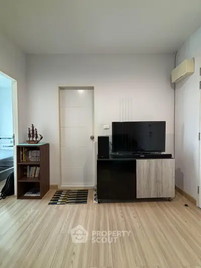Modern living room with sleek TV stand and wooden flooring, adjacent to a cozy bedroom.