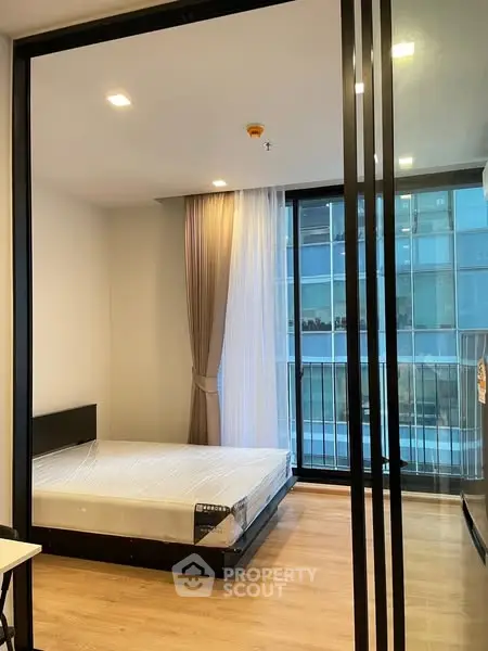 Modern bedroom with floor-to-ceiling windows and balcony view in urban apartment.