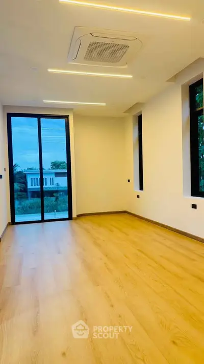 Spacious modern room with wooden flooring and large windows offering natural light and scenic views.