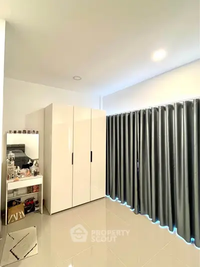 Modern bedroom with sleek wardrobe and vanity, featuring glossy tiles and elegant curtains.