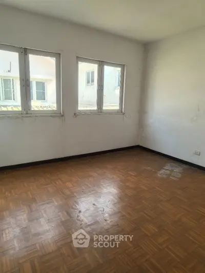 Spacious empty room with parquet flooring and large windows, perfect for customization.