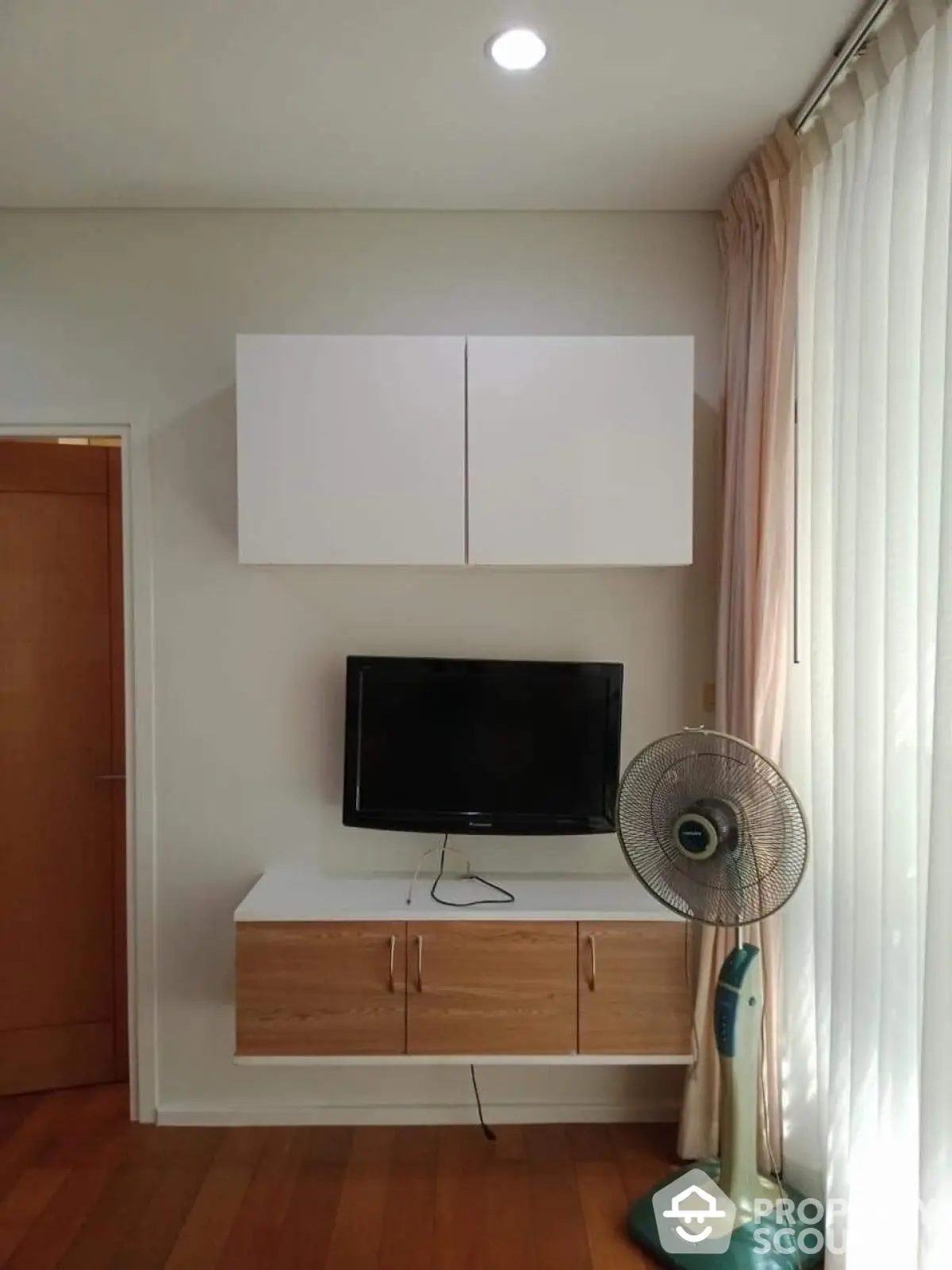 Modern living room corner with TV and fan, wooden flooring, and natural light.