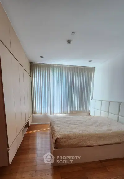 Spacious bedroom with elegant wooden flooring and large window with curtains, perfect for relaxation.