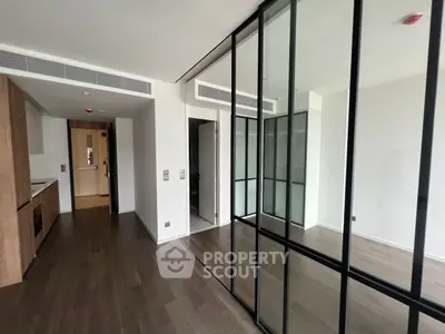 Modern apartment interior with glass partitions and wooden flooring, featuring a sleek kitchen area.