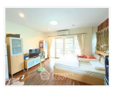 Spacious bedroom with wooden flooring and natural light