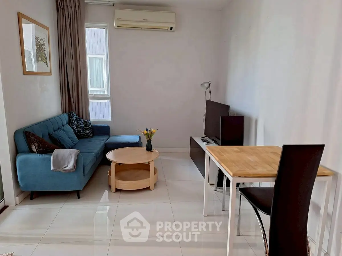 Modern living room with blue sofa, TV, and dining table in cozy apartment.