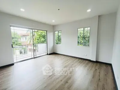 Spacious living room with large windows and balcony access, featuring elegant wood flooring.