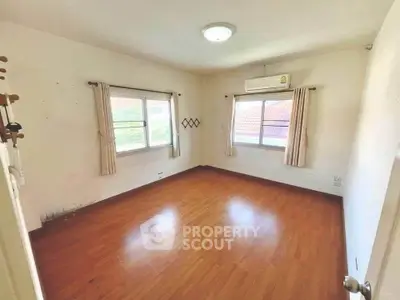 Spacious empty room with wooden flooring and large windows, perfect for customization.