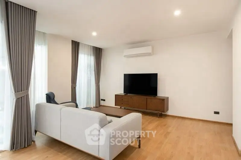 Modern living room with sleek furniture and large TV, featuring elegant curtains and wooden flooring.