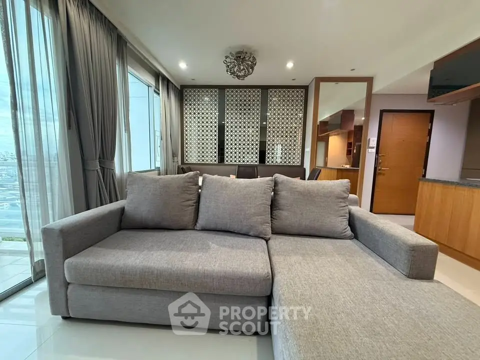 Spacious living room with modern gray sofa and large windows offering stunning city views.