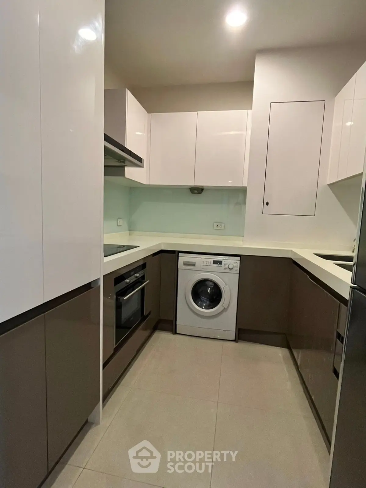 Modern kitchen with sleek cabinetry and built-in appliances, featuring a washing machine and oven.