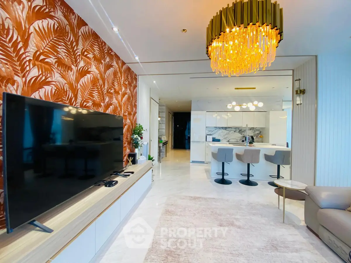 Luxurious living room with modern decor and open kitchen layout, featuring a stylish chandelier and large TV.
