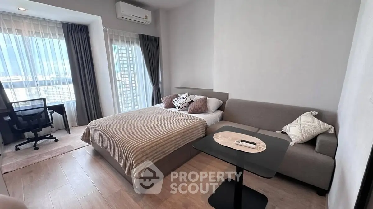 Modern bedroom with cozy bed, sofa, and city view from large windows