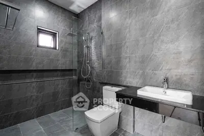 Modern minimalist bathroom with sleek gray tiles and glass shower enclosure.
