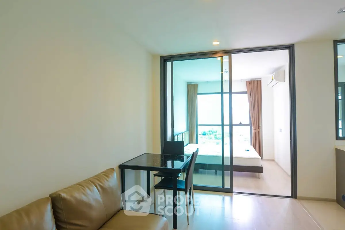 Modern apartment interior with glass partition, cozy living area, and bright bedroom view.