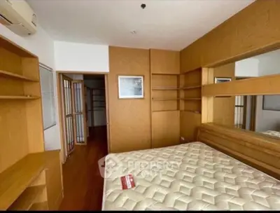 Spacious bedroom with wooden accents and built-in shelves, featuring a comfortable mattress.
