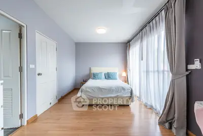 Spacious bedroom with large windows and elegant curtains, featuring a cozy bed and wooden flooring.