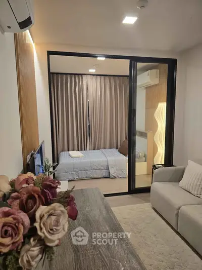 Modern apartment interior with cozy living room and stylish bedroom separated by glass partition.