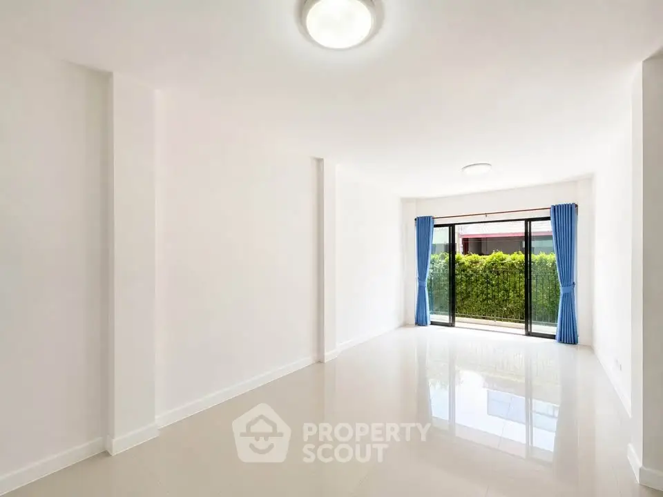 Spacious empty living room with large windows and blue curtains, overlooking a lush garden.