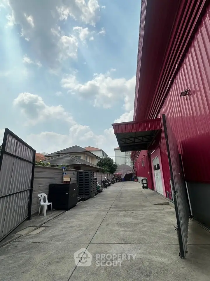 Expansive industrial property with red exterior and spacious driveway under a bright sky.
