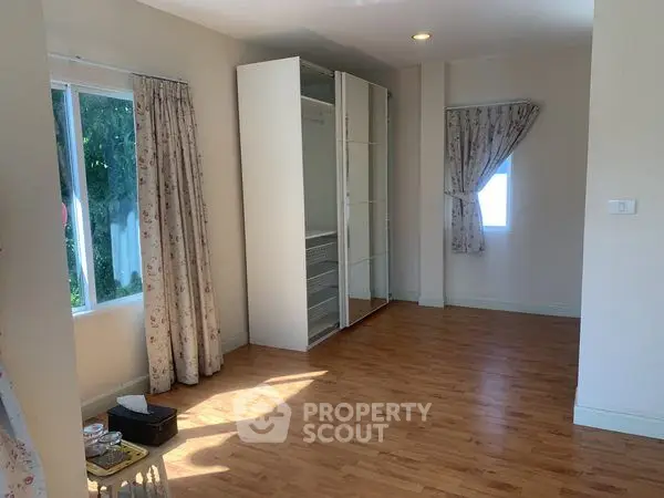 Spacious bedroom with wooden flooring and large windows for natural light.