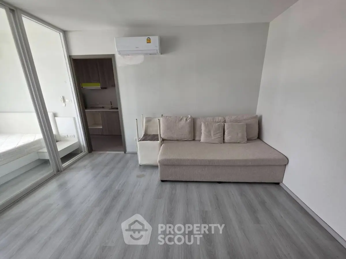 Modern living room with sleek flooring and cozy sofa, adjacent to a bright bedroom.