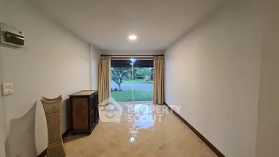 Spacious empty room with large sliding glass doors opening to a lush garden view.