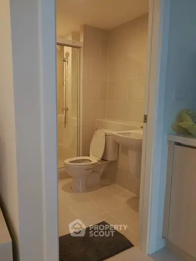 Modern bathroom with sleek design and neutral tiles, featuring a shower and toilet in a compact space.
